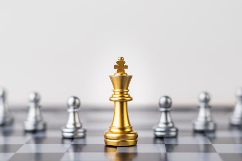 Gold Chess king figure on Chessboard and surrounded by a number of fallen silver chess pieces against opponent or enemy.